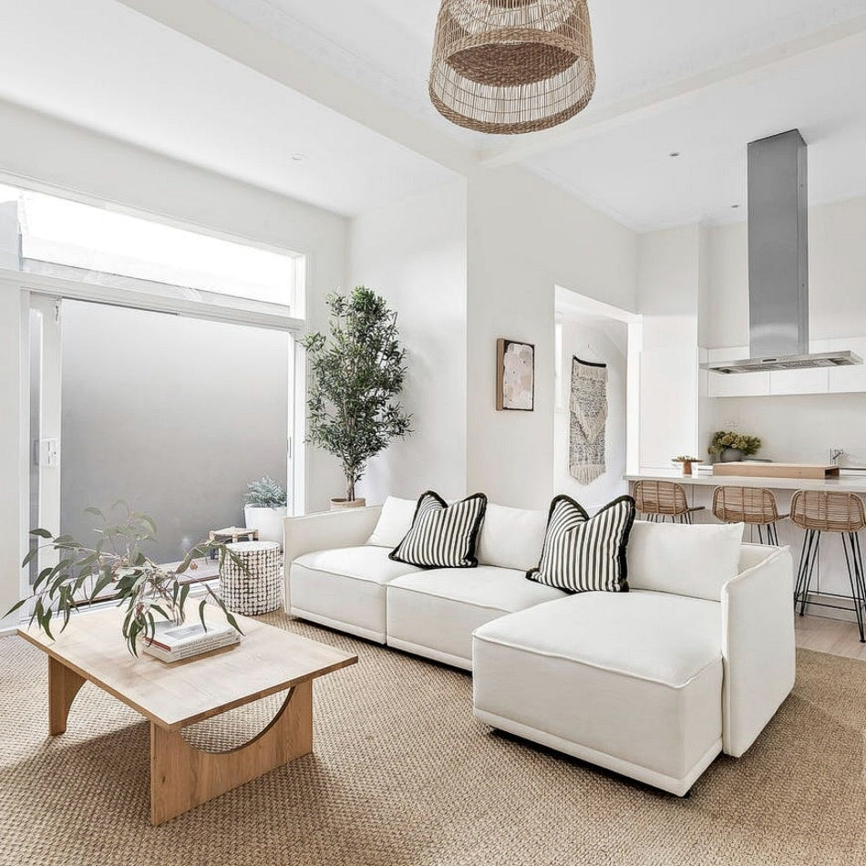 A bright, refined living room with heavy rustic river rock natural fibre flooring, a white sectional and a wooden coffee table.