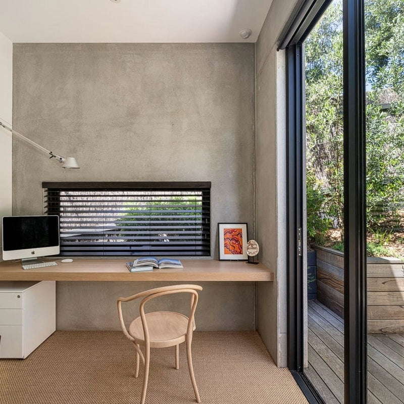 A bright home office with a wood desk, framed art, and a natural fibre sisal rug near glass doors in an elegant, styled interior.