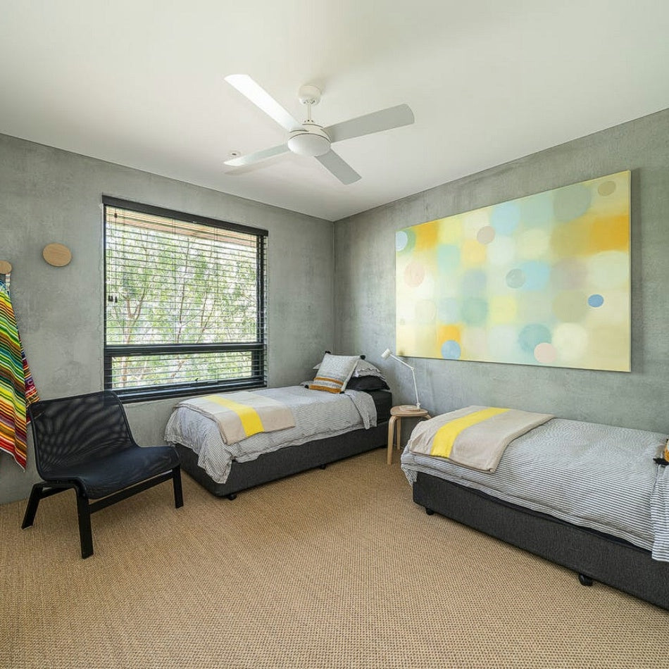 Elegant bedroom featuring twin beds, black accent chair, abstract art, and a refined natural sisal floor in a styled interior.