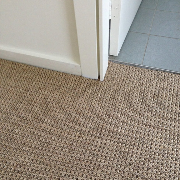 A doorway reveals a transition from textured sisal flooring in warm autumn tones to sleek, smooth gray tiles in a refined interior.