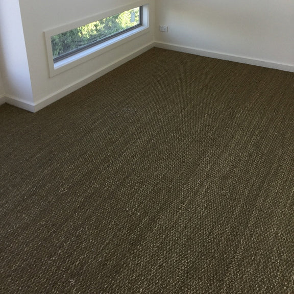 Sunlit room featuring elegant basketweave seagrass flooring, crisp white walls, and a window framing lush garden views.