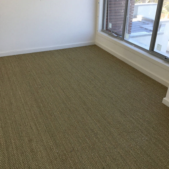 A spacious, light-filled room with crisp white walls and elegant basketweave seagrass flooring in a refined natural finish.