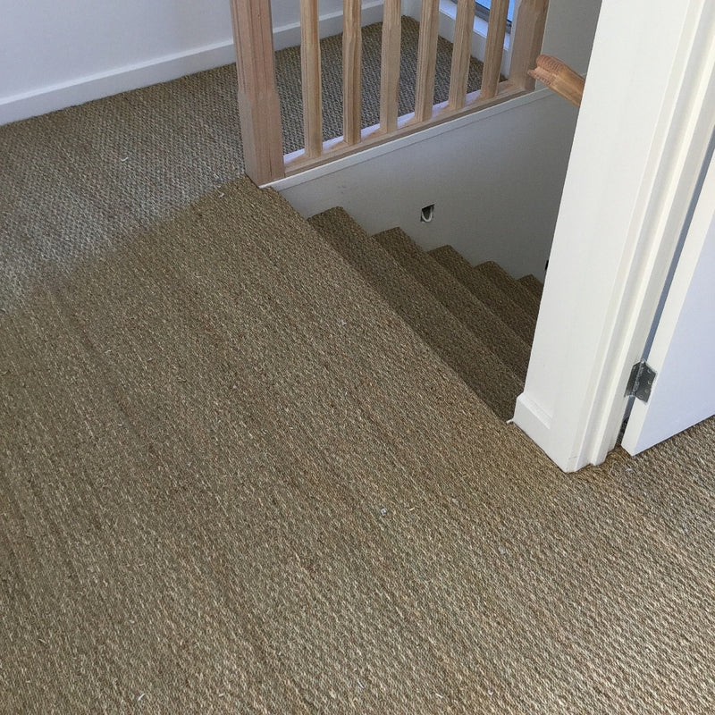 Basketweave seagrass carpet graces the stairs, complemented by a light wood railing in a refined, contemporary home setting.