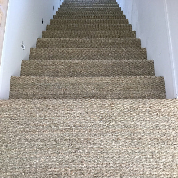 Elegant beige stairs with crisp white walls, highlighted by textured basketweave seagrass flooring in a refined interior.