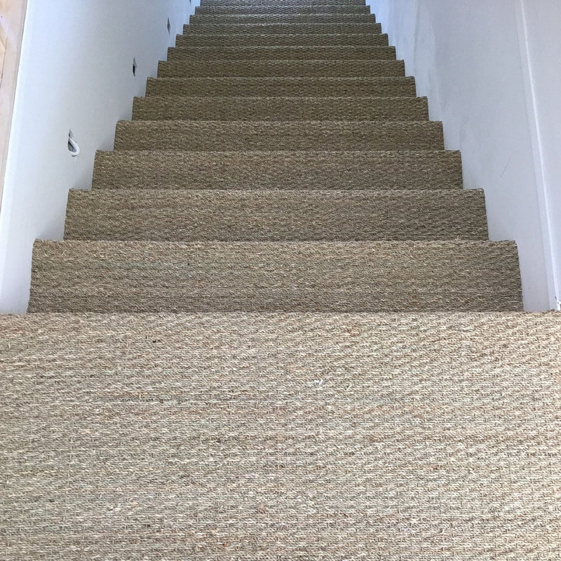 Elegant beige stairs with crisp white walls, highlighted by textured basketweave seagrass flooring in a refined interior.