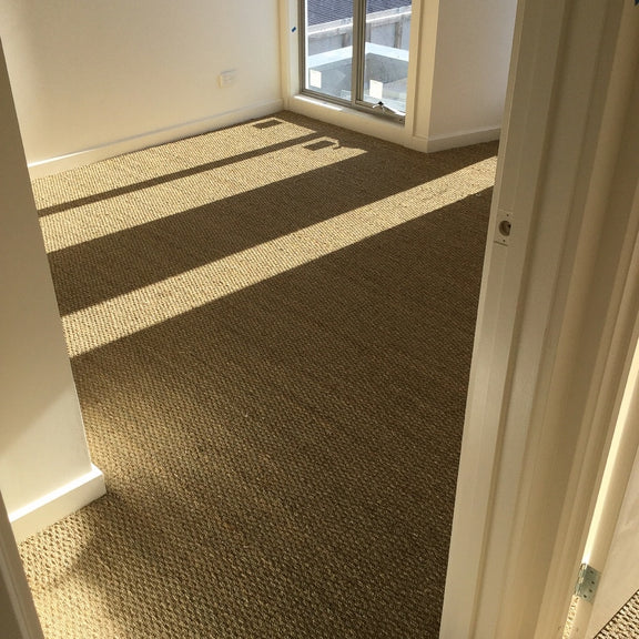 A bright, airy room featuring textured basketweave seagrass carpet, crisp white walls, and modern sliding glass doors.