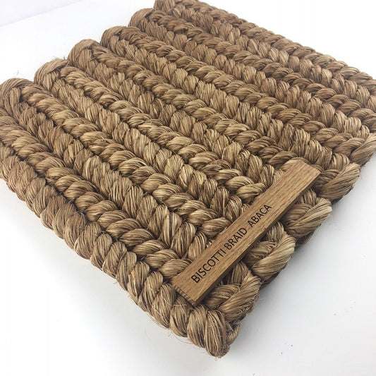 Intricately braided biscotti-toned natural fibre mat, showcasing rich texture and a subtle wooden tag on the corner.