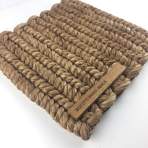 Intricately braided biscotti-toned natural fibre mat, showcasing rich texture and a subtle wooden tag on the corner.