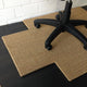 A tan, cross-shaped sisal chair pad sits beneath a black office chair on hardwood flooring in a refined, modern workspace.