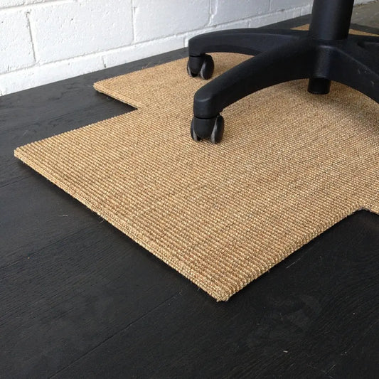 A wheeled office chair rests on a finely woven sisal chair pad, showcasing natural texture against a dark timber floor.