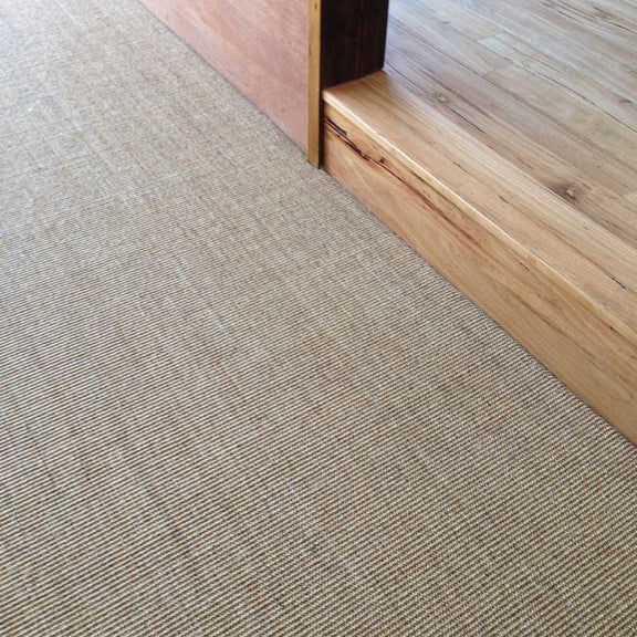 Fine ribbed sisal carpet precisely meets natural wood flooring at a step, highlighting a refined materials transition.