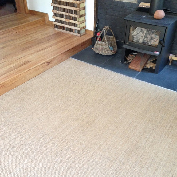 A wood stove with stacked firewood sits beside a fine ribbed sisal rug on warm timber floors in an elegantly styled interior.