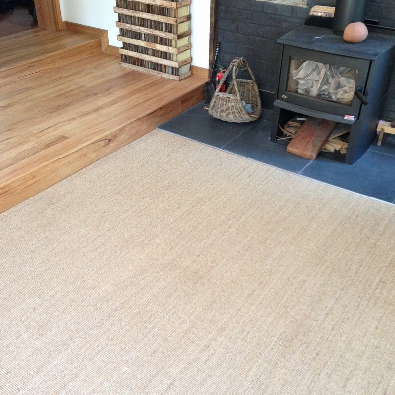 A wood stove with stacked firewood sits beside a fine ribbed sisal rug on warm timber floors in an elegantly styled interior.