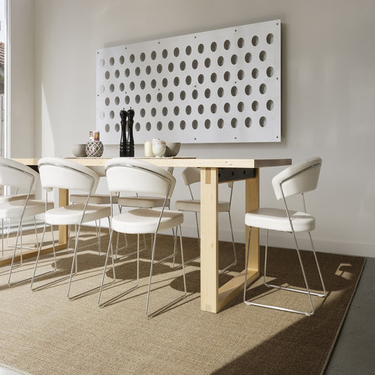 A contemporary dining room with a wooden table, white chairs, and a fine ribbed sisal rug grounded on timber flooring.