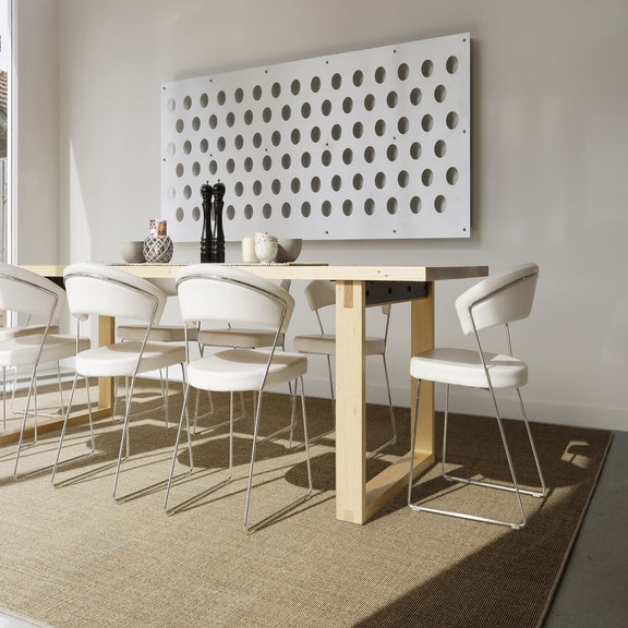 A contemporary dining room with a wooden table, white chairs, and a fine ribbed sisal rug grounded on timber flooring.