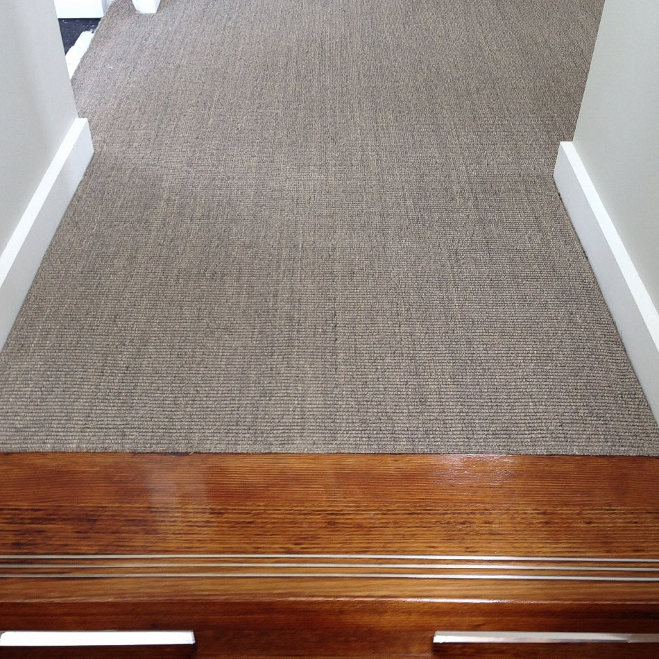 A hallway with fine ribbed granite sisal flooring transitions seamlessly to polished wood, complemented by crisp white walls.