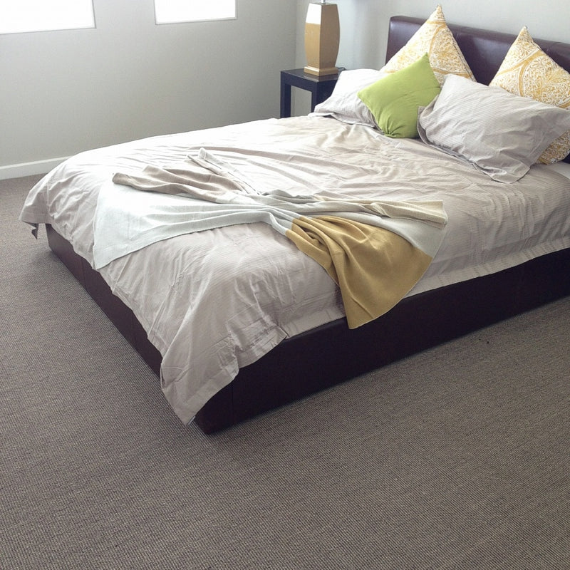 A contemporary bedroom features a neatly made bed atop fine ribbed granite sisal carpet, highlighting natural texture and refined style.