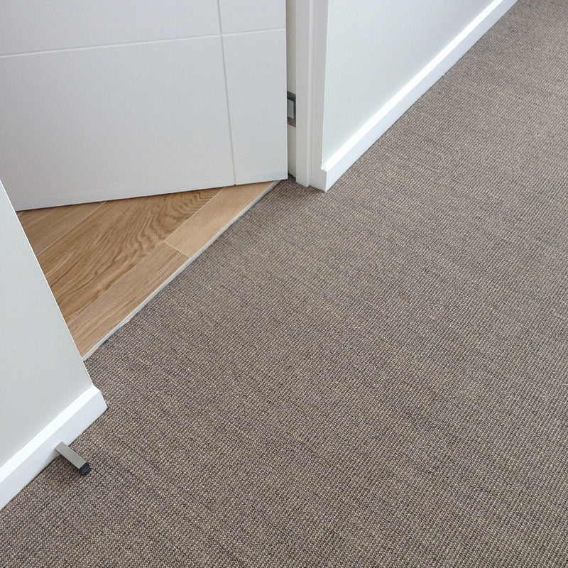 A fine ribbed granite sisal rug meets pale timber floors at an open doorway, framed by crisp white walls in a serene interior.