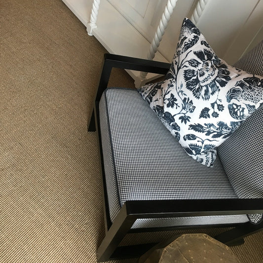 A black checkered armchair rests on fine ribbed quartz sisal flooring beside a sleek white cabinet in a thoughtfully styled space.