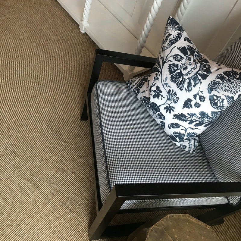 A black checkered armchair rests on fine ribbed quartz sisal flooring beside a sleek white cabinet in a thoughtfully styled space.