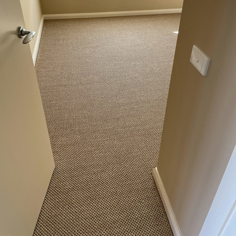An open door reveals a sunlit room with beige walls and beautifully textured natural sisal flooring, highlighting crafted quality.