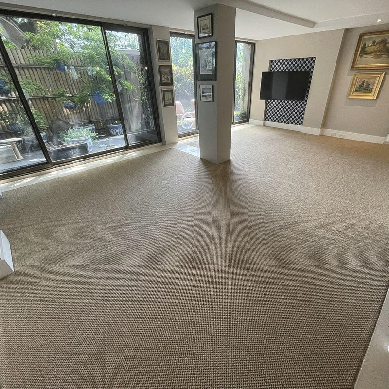 Spacious living room with a textured granite sisal rug, abundant natural light from tall windows, and curated framed artwork.