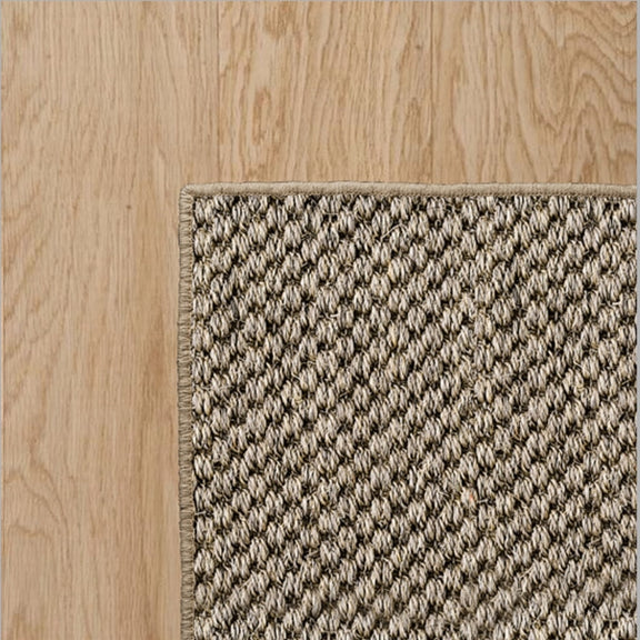 Overlock border rug in a natural fibre, showcased on light timber flooring for an elegant, refined interior finish.