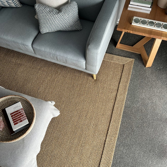 A stylish living room featuring a grey sofa, textured pillows, and a self-edged natural fibre rug on hardwood flooring.