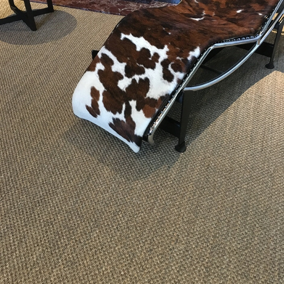 A cowhide and metal chaise lounge sits atop rich, textured slate-grey sisal flooring in a refined, contemporary living space.