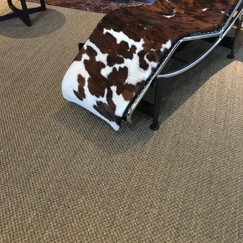 A cowhide and metal chaise lounge sits atop rich, textured slate-grey sisal flooring in a refined, contemporary living space.