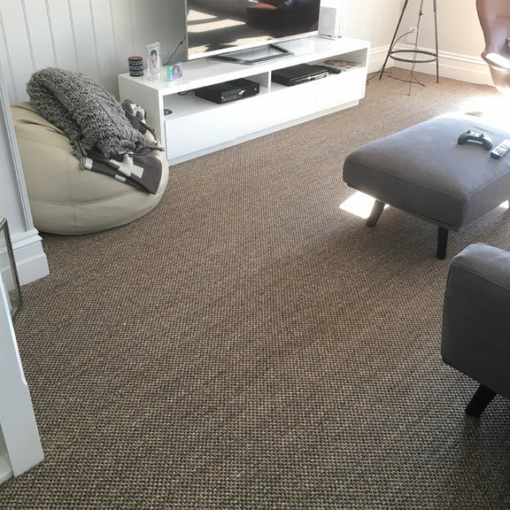 A contemporary living room featuring a white TV stand, bean bag, gray ottoman and a luxurious slate-toned sisal rug on natural floors.