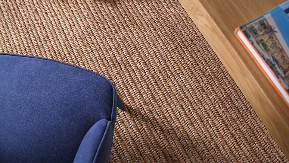 A blue accent chair sits on a premium natural fibre rug beside a wooden table topped with a book in an elegantly styled interior.