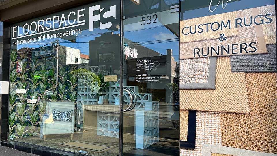 A refined storefront window showcases artisanal natural fibre rugs, curated flooring samples, and an elegant open hours display.