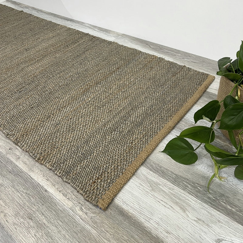 A frost grey runner sits on pale timber floors next to a leafy green plant in a clay pot, styled in a bright, modern interior.