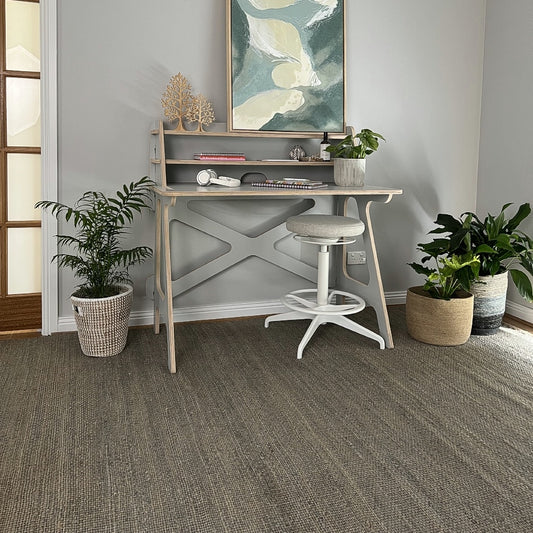 A small, modern home office styled with a sleek desk, greenery, abstract art and a finely woven Frost Grey jute rug.