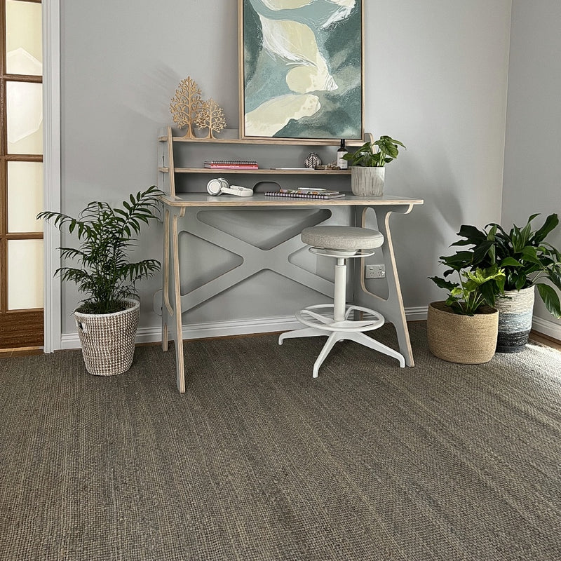A small, modern home office styled with a sleek desk, greenery, abstract art and a finely woven Frost Grey jute rug.