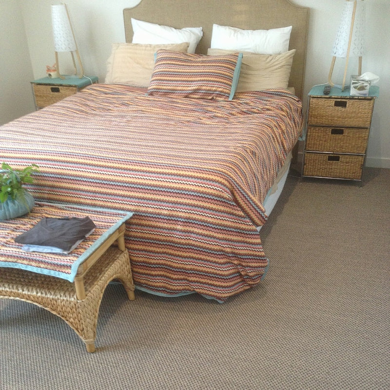 A serene bedroom with a striped bedspread, dual nightstands, and a fine sisal rug adding warmth and texture to the space.