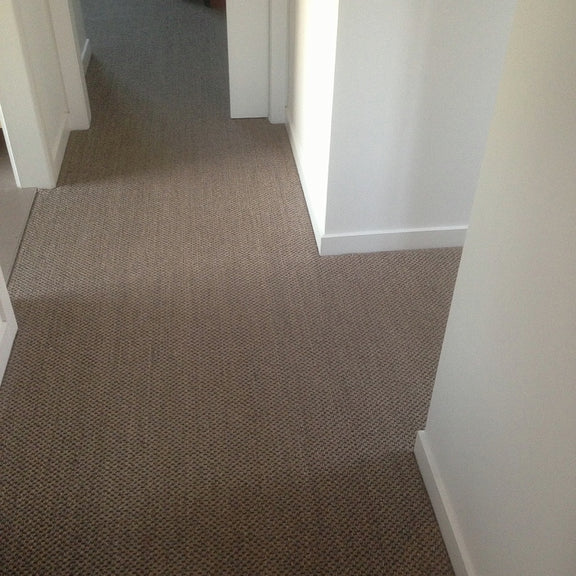 A sunlit hallway features fine rustic granite sisal flooring, white walls, and sleek doorways in a refined home interior.