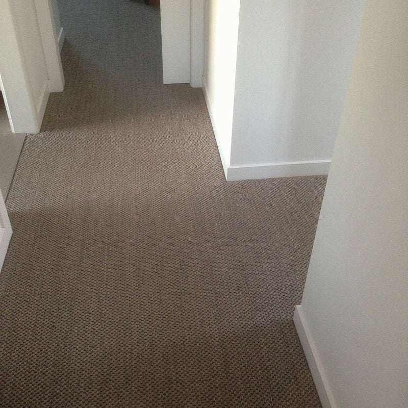 A sunlit hallway features fine rustic granite sisal flooring, white walls, and sleek doorways in a refined home interior.