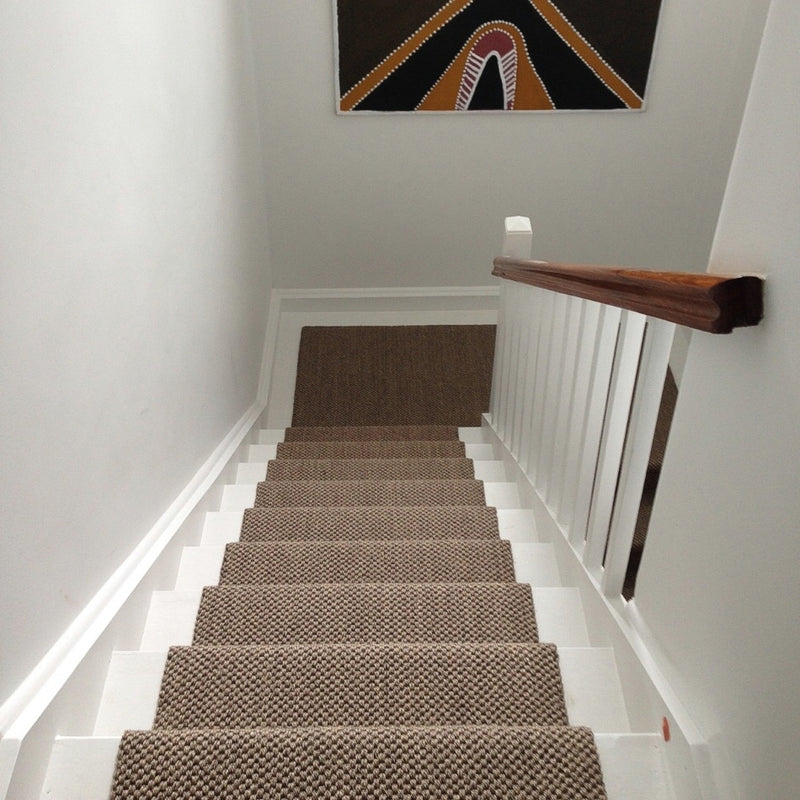 Textured sisal carpet in a refined granite tone covers stairs with a sleek white railing, leading up to an airy, light-filled landing.