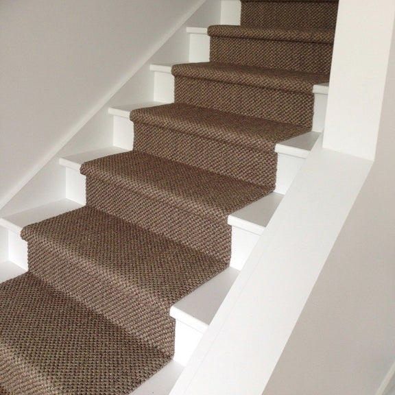 A textured sisal runner in a granite hue elevates crisp white wooden stairs, framed by smooth white walls for a refined look.
