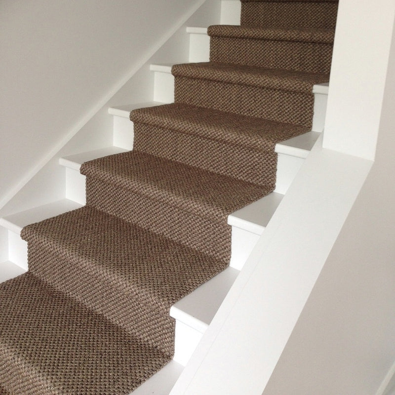 A textured sisal runner in a granite hue elevates crisp white wooden stairs, framed by smooth white walls for a refined look.