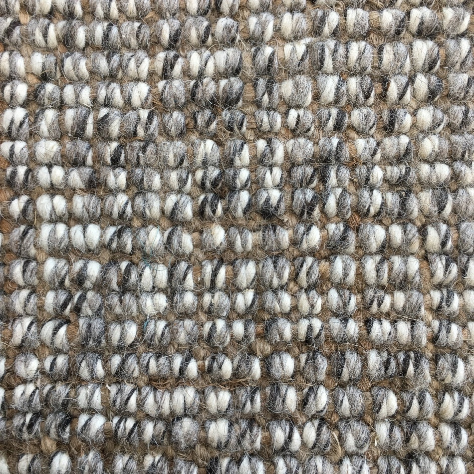 Thick, textured loops of beige, white, brown and gray wool and jute fibres create a refined, natural woven surface.