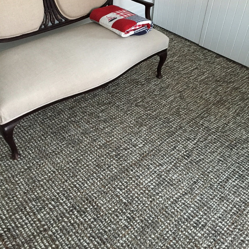 A beige cushioned bench topped with a neatly folded quilt rests on a textured wool and jute rug in an elegantly styled living space.