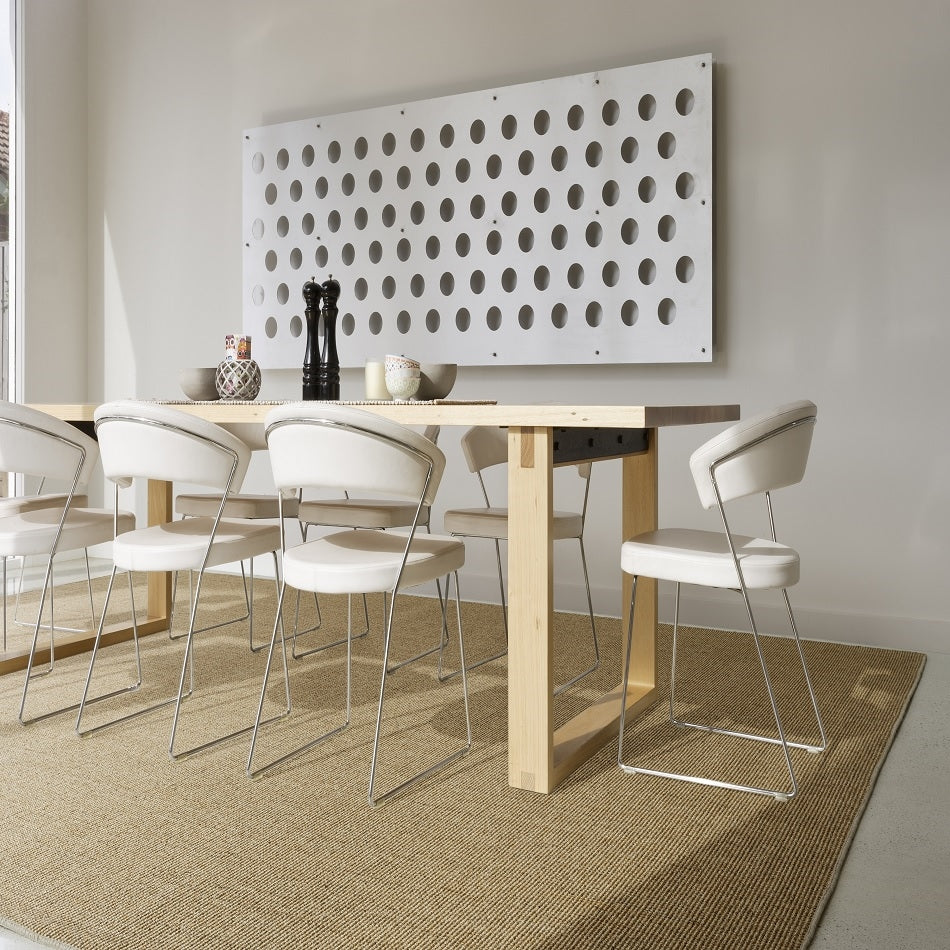 A contemporary dining space with a wooden table, white chairs, elegant wall art and a textured sisal rug in a styled home interior.