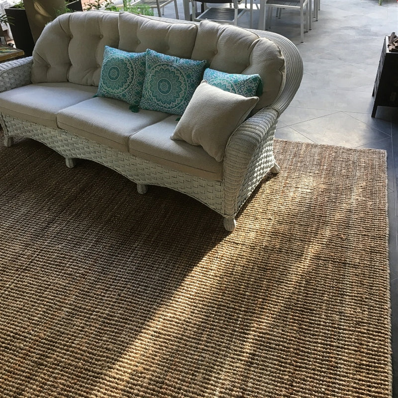 A wicker sofa with plush blue and neutral cushions rests on a natural jute rug, paired with a dining table in a serene living space.