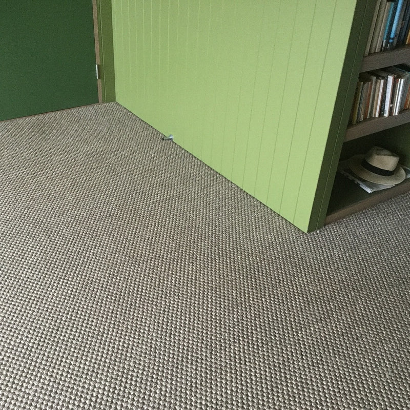 An open green door beside a bookshelf and hat, revealing durable granite-hued sisal flooring in a thoughtfully styled interior.