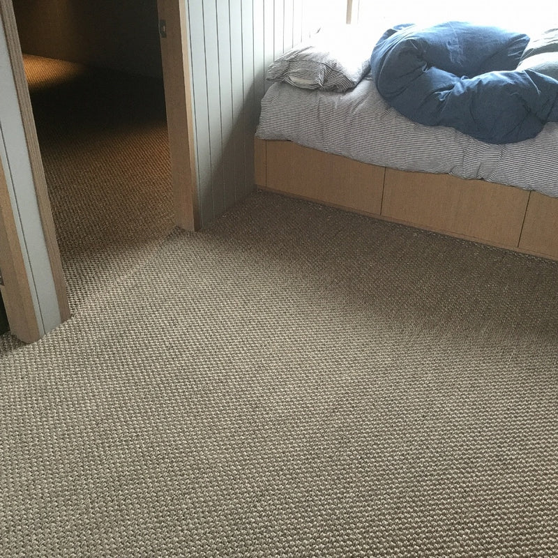 Blue bedding on an unmade bed next to a rustic granite-hued sisal rug in a softly lit, tastefully styled bedroom.