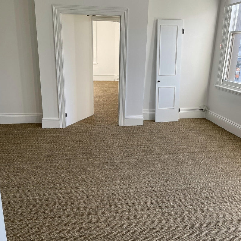 Herringbone seagrass flooring in a bright room with white walls, windows, closet door and open doorway, styled for modern living.