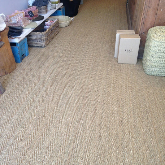 Beige herringbone seagrass carpet with woven baskets and soft rosé boxes, styled in a refined, contemporary interior.